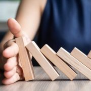 115772386_s Businesswoman hand Stopping Falling wooden Dominoes. Business, Risk Management, Solution and strategy Concepts